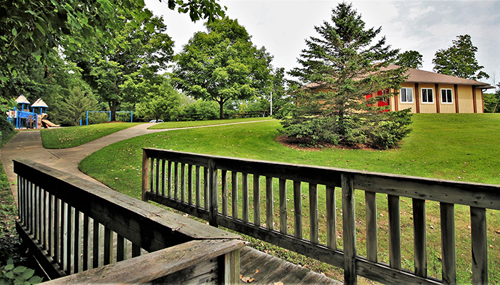 A small bridge leads to a sidewalk that splits in two directions -- One point leads to a playground, and another leads to the day-use building.