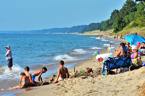 Families play in the sand and wade in the waters at Kirk Beach on a sunny summer afternoon