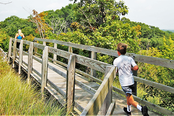 A child runs along a boardwalk that runs through a wooded area