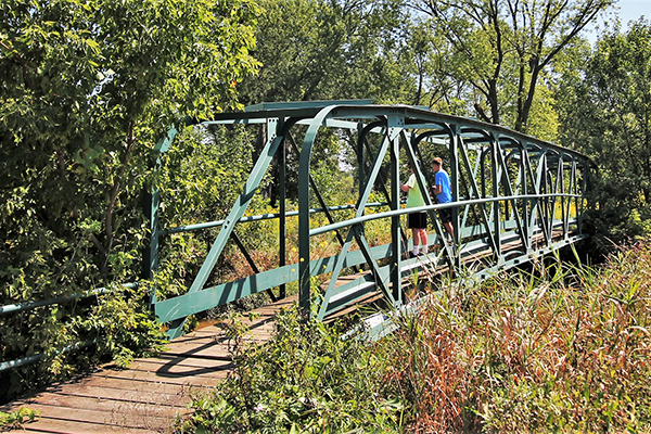 Two young men stand in the middle of a pedestrian bridge and look out over a wooded area