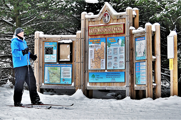 A man in skis stands in front of the snow-covered park information kiosk