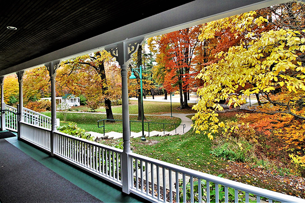 A view from the porch of the Weaver House; A sidewalk leads down a small hill to a parking lot surrounded by trees in autumn.