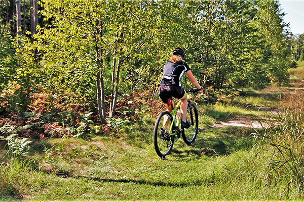 A woman bikes down a grassy path through a wooded area